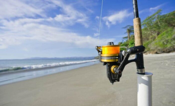 Surf fishing spinning reel setup on sandy beach with ocean waves