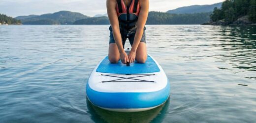 Beginner balancing on a Niphean paddle board in calm water